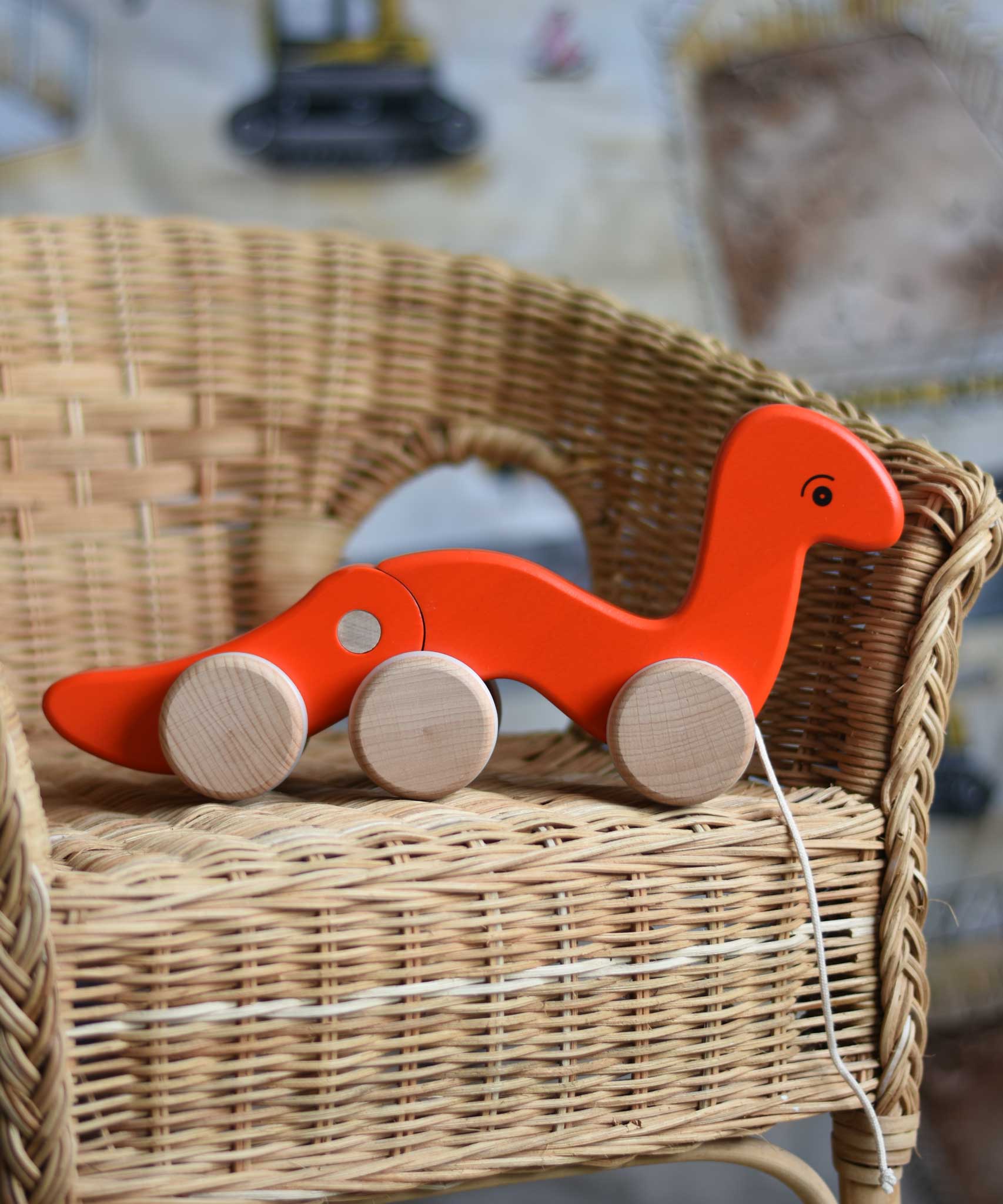 A red Bajo wriggling worm pull along toy placed on a child's wicker chair. These heirloom quality toys by Bajo are part of a wide range of wooden toys available here at Babipur.  