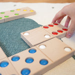 Close up of a hand moving the Bajo XXL wooden dominos on a blue and white carpet