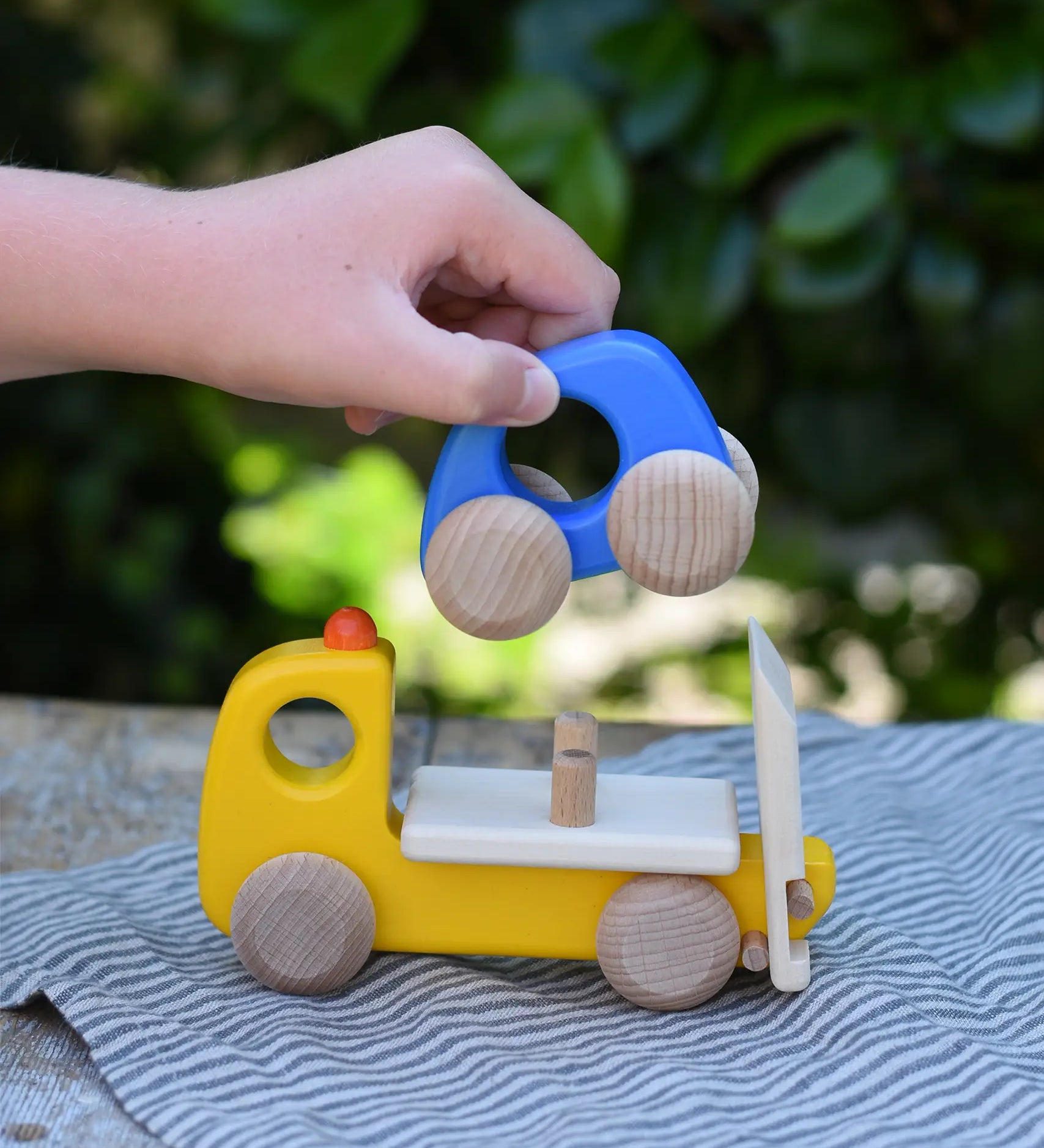 Bajo yellow breakdown lorry wooden toy with a child's hand lifting the blue car off the trailer.