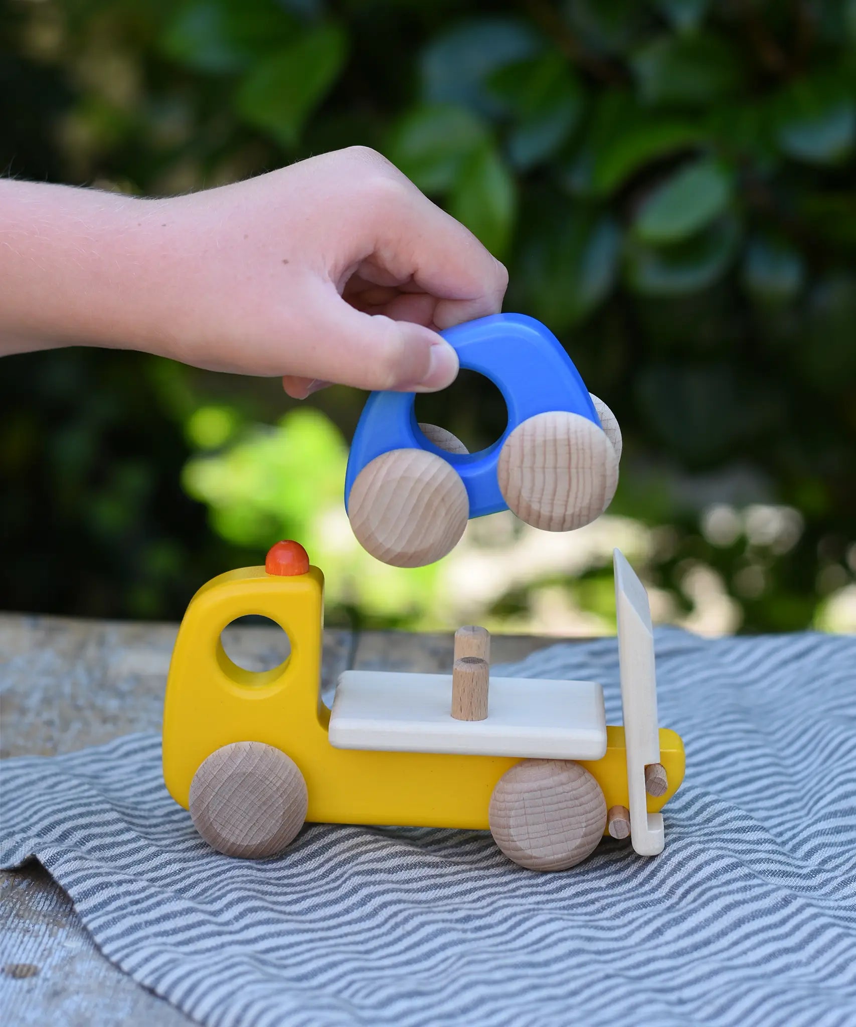 Bajo yellow breakdown lorry wooden toy with a child's hand lifting the blue car off the trailer.