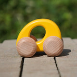 Bajo handmade wooden ellipse toy car in yellow with unpainted wheels standing on a concrete surface