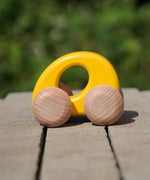 Bajo handmade wooden ellipse toy car in yellow with unpainted wheels standing on a concrete surface