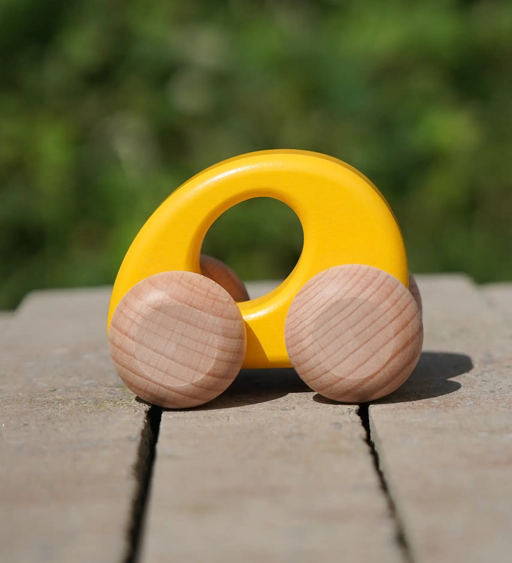 Bajo handmade wooden ellipse toy car in yellow with unpainted wheels standing on a concrete surface