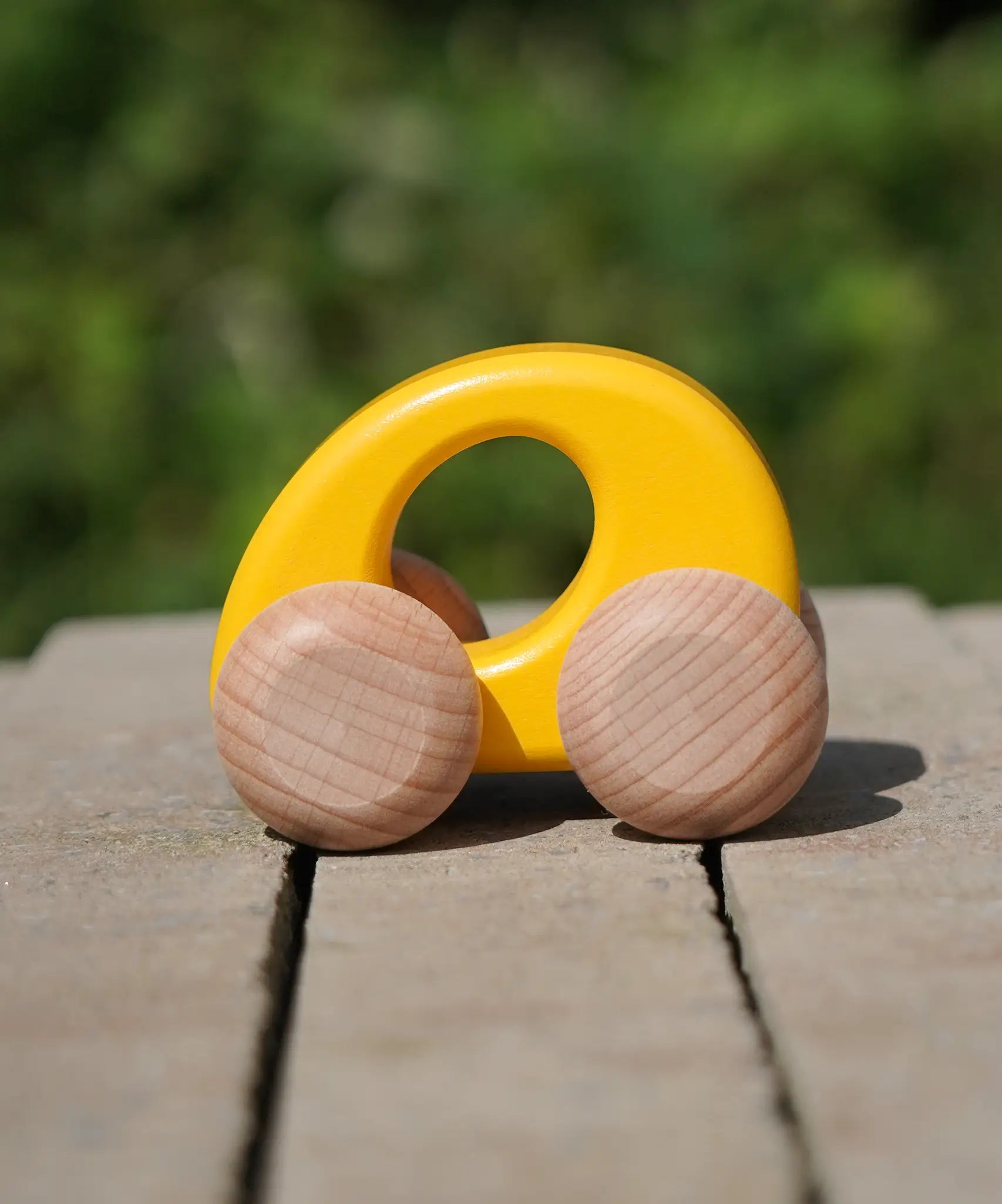 Bajo handmade wooden ellipse toy car in yellow with unpainted wheels standing on a concrete surface