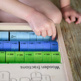 Bajo Fraction Set Maths Resource Learning Toy showing child's hand picking the fraction blocks from inside the wooden fractions box