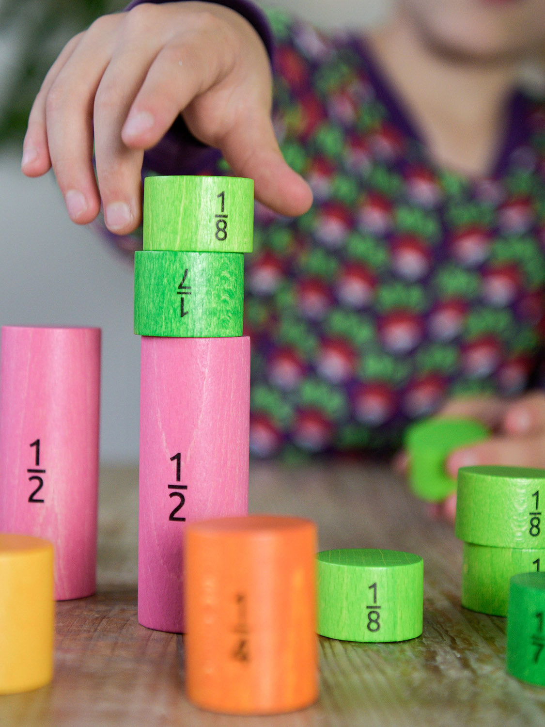 Bajo Fraction Set Maths Resource Learning Toy showing child's hand playing with the fraction blocks on a wooden table