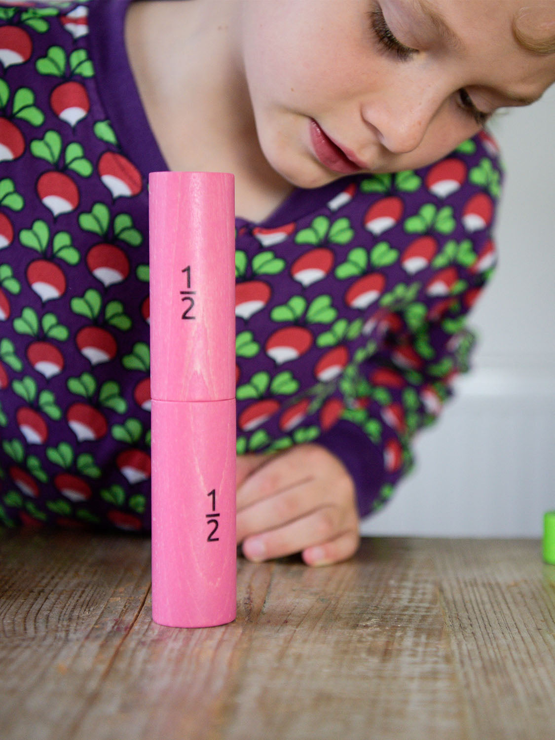 Bajo Fraction Set Maths Resource Learning Toy showing child looking and playing with two 1/2 fraction blocks on a wooden table