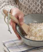 A Bambu Bamboo Rice Paddle in a bowl of rice being held by a person. 