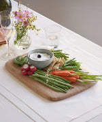 Close up view of the large Bumbu bamboo serving and cutting board on a white table cloth with various foods on top and showing the bamboo detail