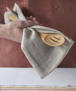 A close up of a person holding a Bambu Bamboo Give It A Rest Slotted Spoon with a linen cloth in their hand.  