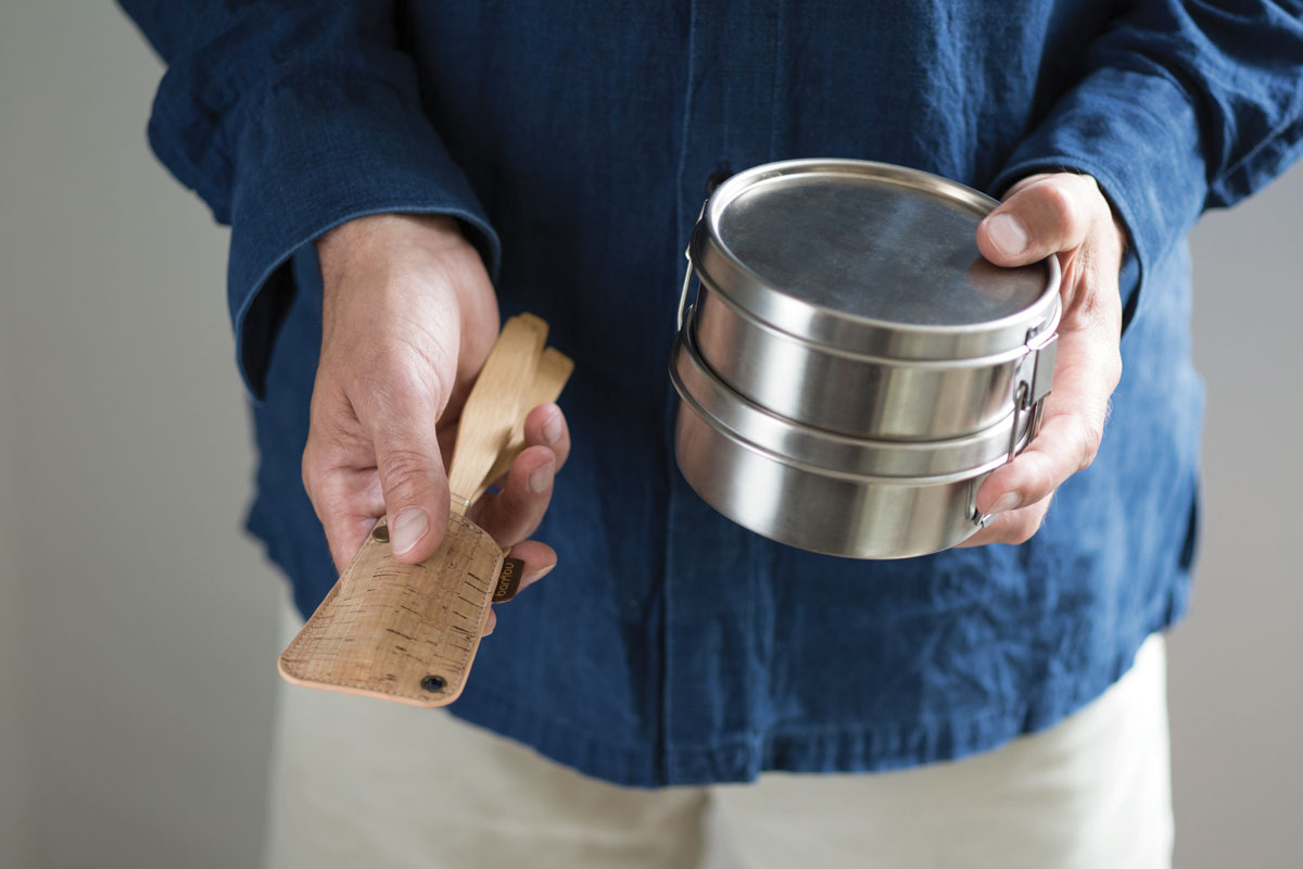 A person holding the Bambu Bamboo Utensil Travel Set with Cork Fabric Pouch with a metal food tin