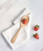 A Bambu Serving Spoon placed on a white linen cloth with a strawberry on it. 