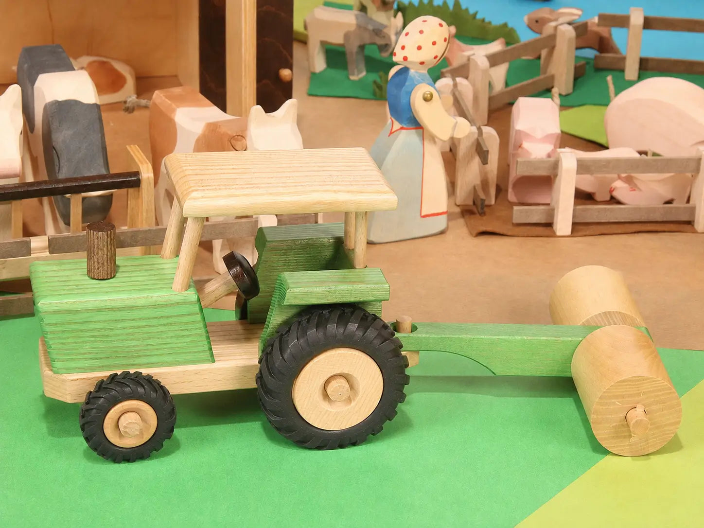 Beck Holzspielzeug traditional wooden toy tractor pulling farm roller attachment in small-world play scene with Ostheimer animal figures.