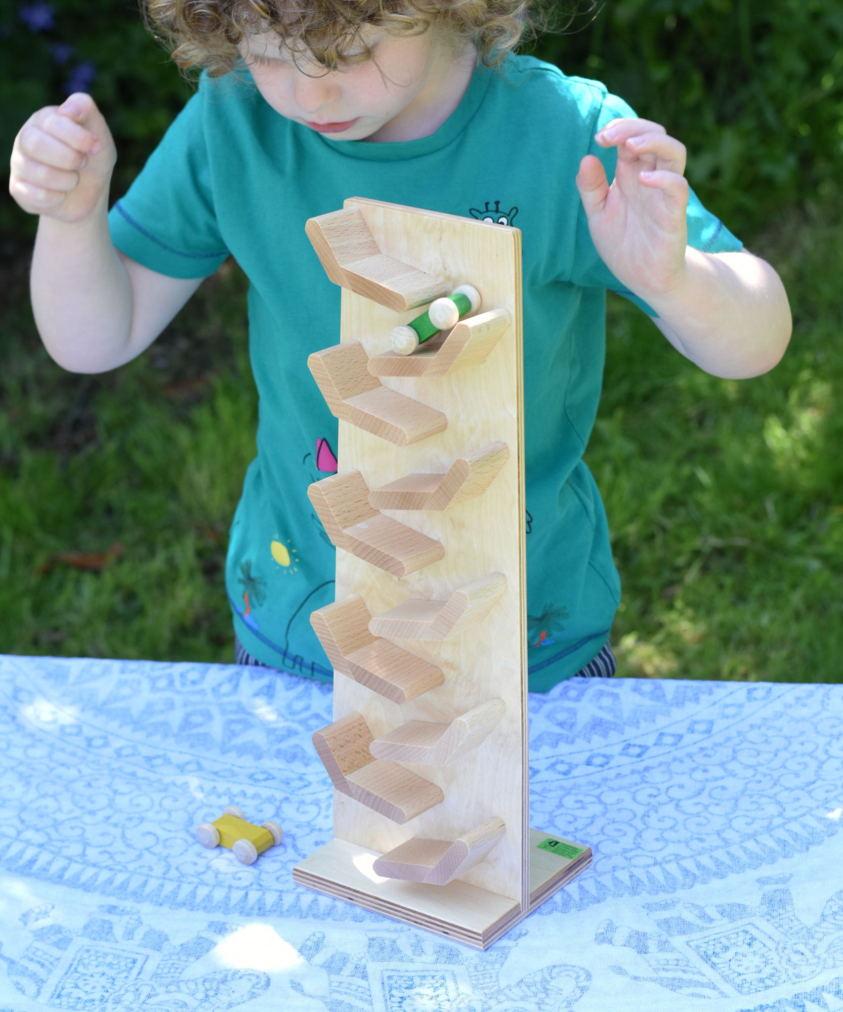 A child playing with the Beck Toys Beechwood Cascading ‘Tower Running Track’ with Race Cars. The child has placed the green coloured race car on the track and has his hands held up in anticipation whilst he watches the car zoom down the track.