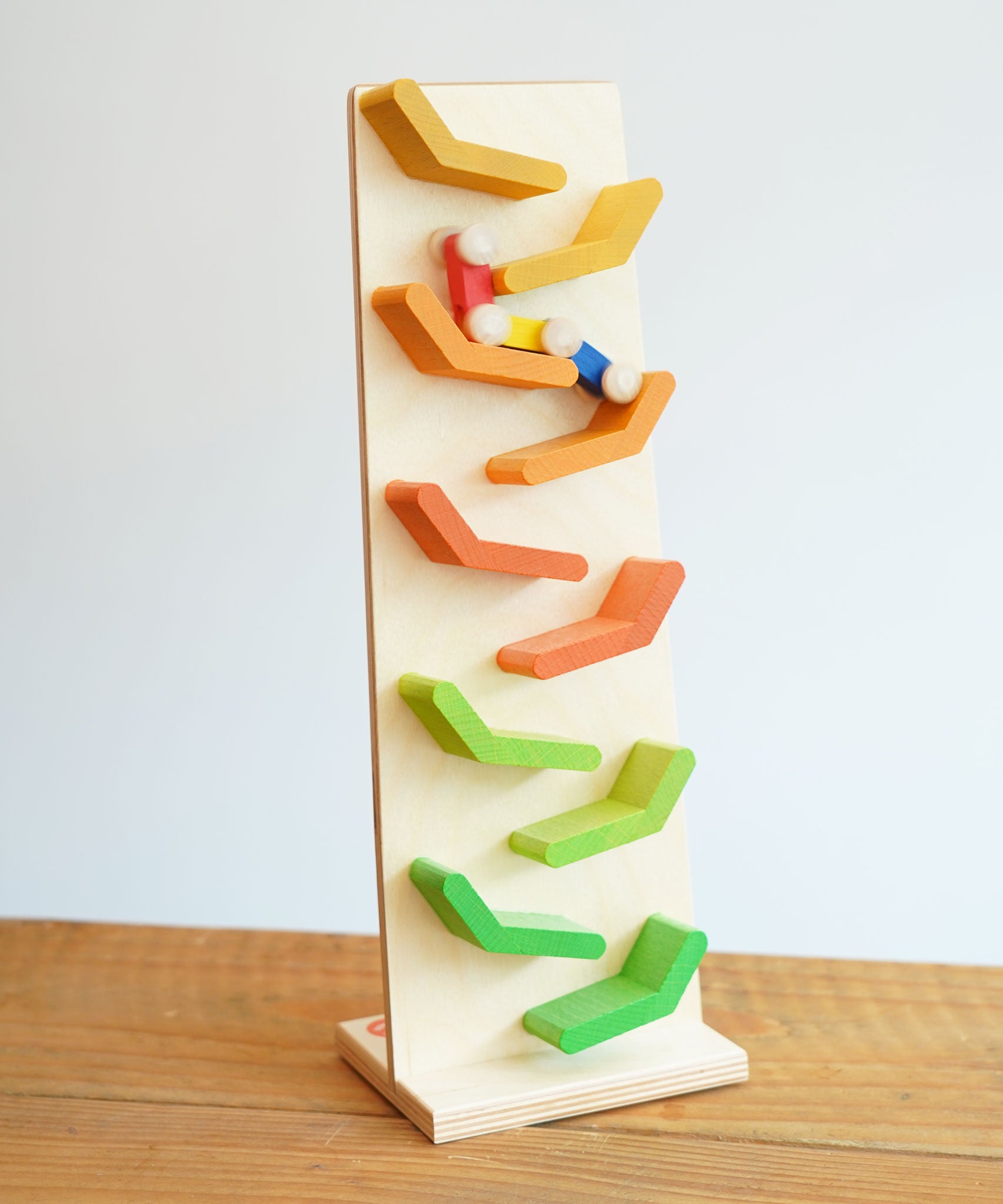 The Beck Toys Beechwood Cascading Tower Running Track with colourful Millipede Car Train placed on a wooden surface. The car train is blurred in motion as it races down teh track.