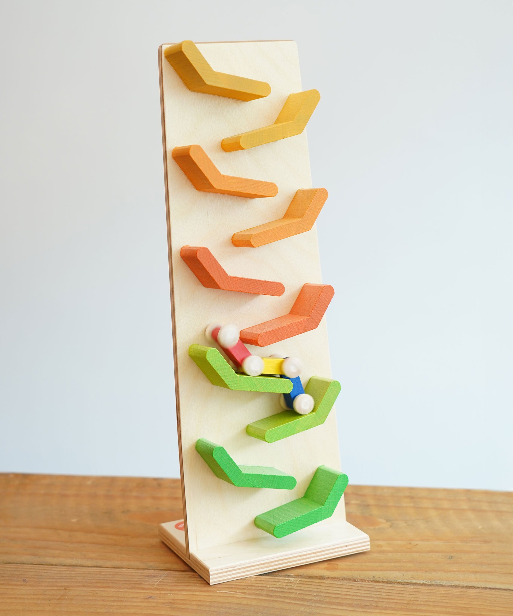 The Beck Toys Beechwood Cascading Tower Running Track with colourful Millipede Car Train placed on a wooden surface. The car train is blurred in motion as it races down teh track.