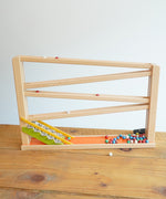 A Beck Toys Chime Marble Run Track  placed on a wooden surface.  The clay marble can be seen cascading down the track. Some of the marbles are blurred in motion.