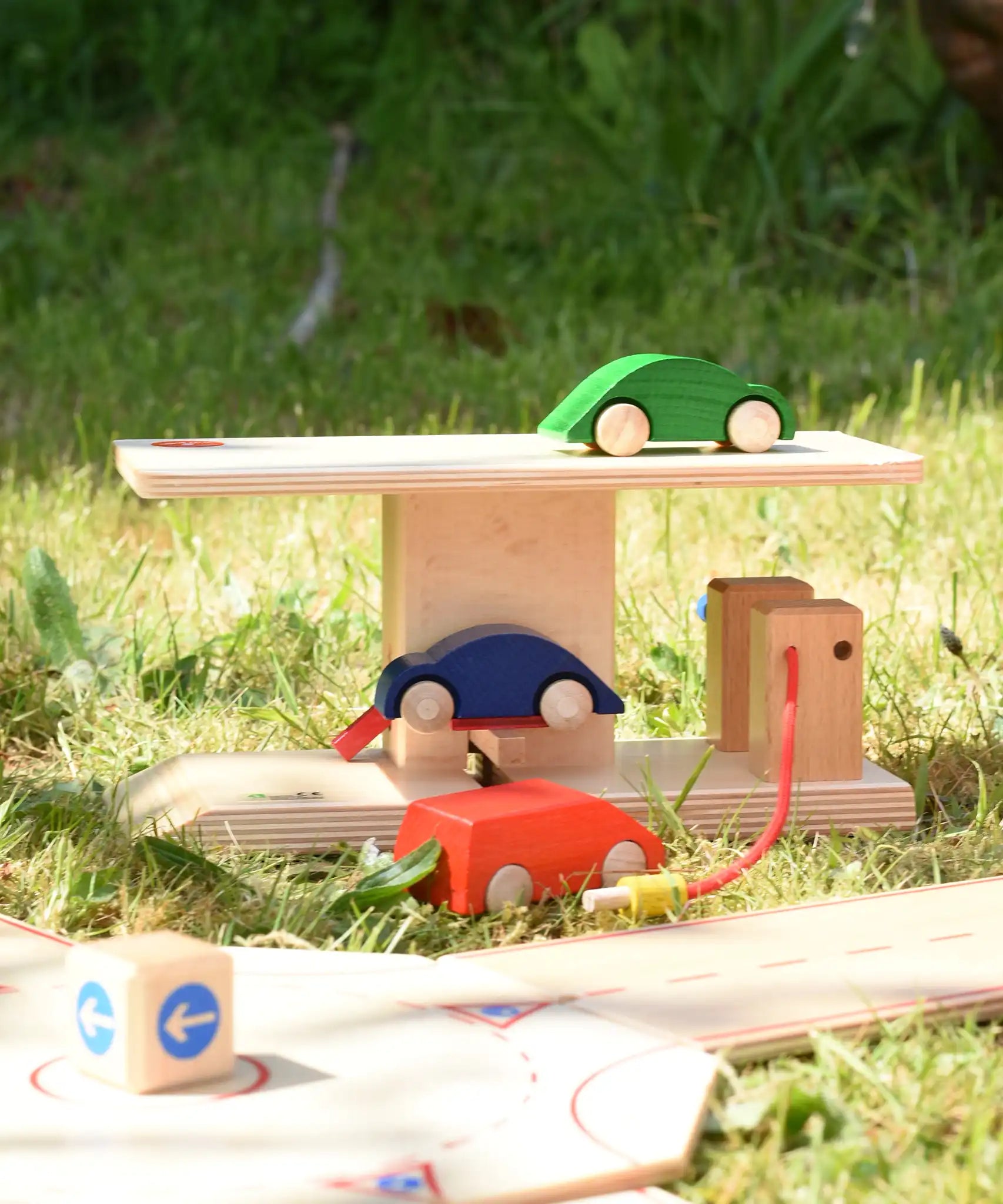 Beck wooden garage & petrol station placed on grass outdoors in front of the roundabout set with wooden cars.