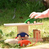 Beck wooden garage & petrol station for toy cars placed on grass outdoors. Child placing wooden car on the roof.