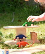 Beck wooden garage & petrol station for toy cars placed on grass outdoors. Child placing wooden car on the roof.