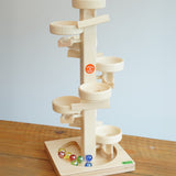 Beck Toys Maple Wood Marble Run Plate Tower placed on a wooden surface. The set comes with 8 coloured glass marbles that can be seen on the base. 