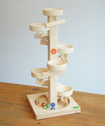 Beck Toys Maple Wood Marble Run Plate Tower placed on a wooden surface. The set comes with 8 coloured glass marbles that can be seen on the base. 