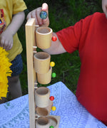 A close up of a child about to place one of the glass marbles in the top cup of the Beck Toys Beech Wood Roller Cup Marble Run.