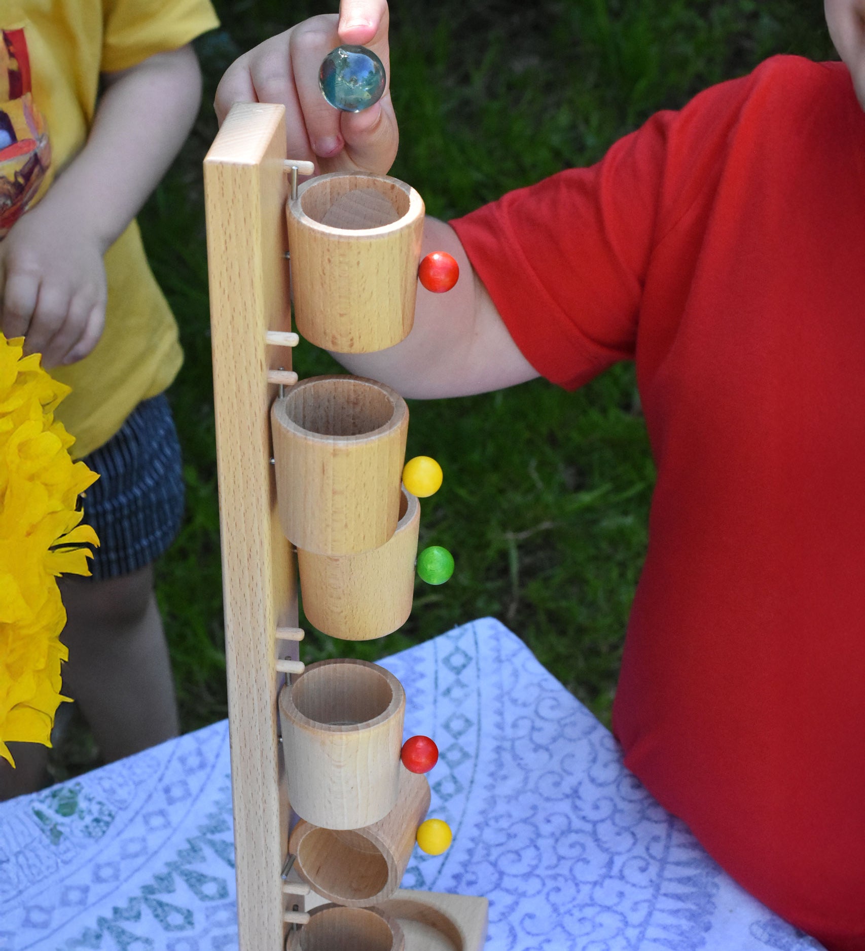 A close up of a child about to place one of the glass marbles in the top cup of the Beck Toys Beech Wood Roller Cup Marble Run.