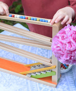 A close up of a child placing a long line of clay marbles at the start of the Beck Toys beech wood Chimes Marble Run Track.