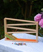 A Christof Beck Spielwaren Toys Chimes Marble Run Track placed on a small table outdoors. The coloured clay marbles have been placed in front of the marble track. 