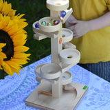 The Beck Marble Run Plate Tower placed on a small table outdoors. The glass marbles have all been placed on the run and can be seen cascading down.