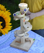 The Beck Marble Run Plate Tower placed on a small table outdoors. The glass marbles have all been placed on the run and can be seen cascading down.
