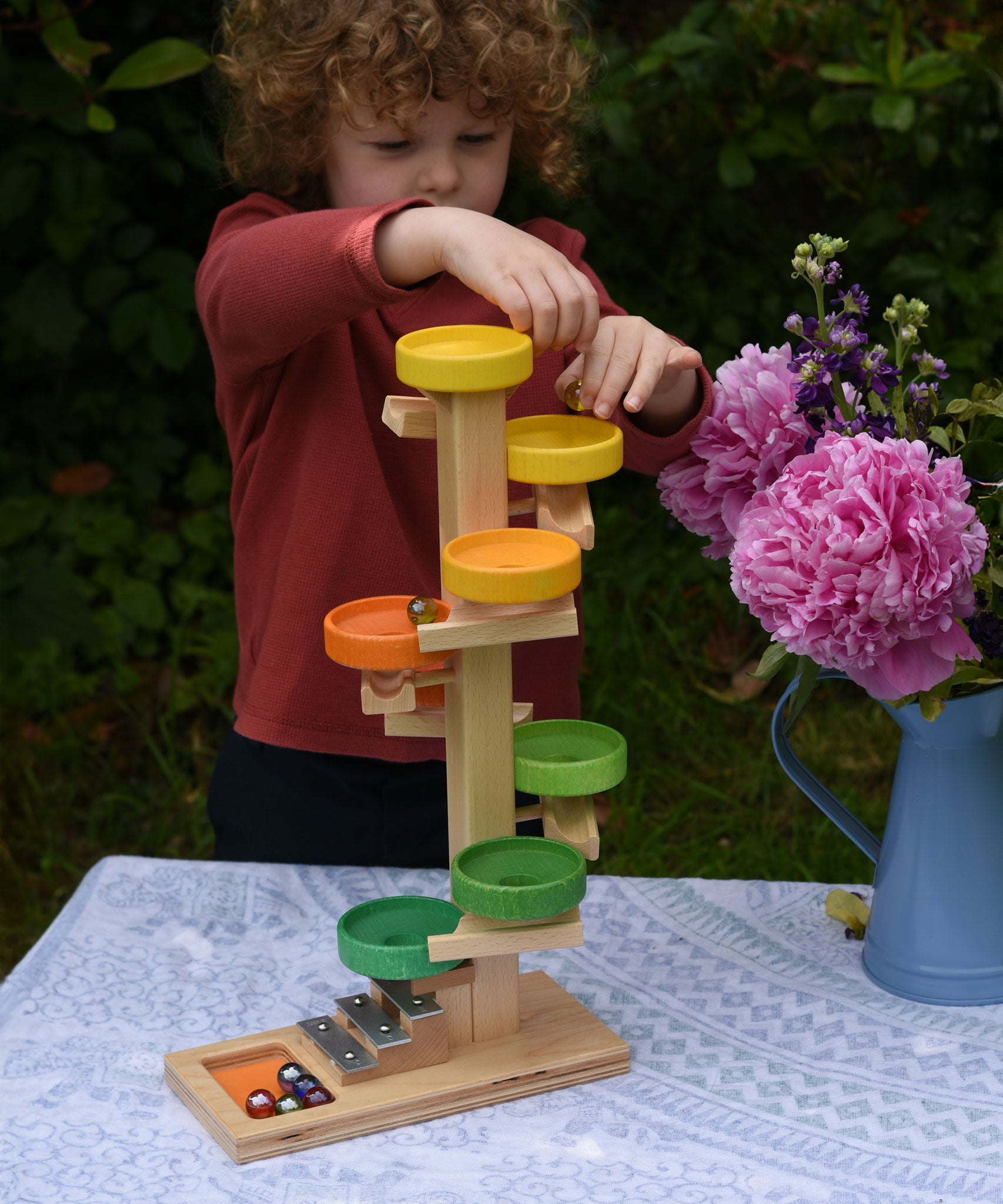 A child placing glass marbles on the top of the Beck Toys Beech Wood Plate Tower Marble Run with Glockenspiel.