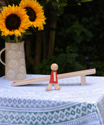 The Beck Toys Nurmi Ramp Walker Wooden Toy placed on a small table outdoors. A vase full of sunflowers has been placed behind the ramp. 