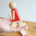 The red colour body walking figure from the Beck Toys Nurmi Ramp Walker Wooden Toy set in an adult's hand.