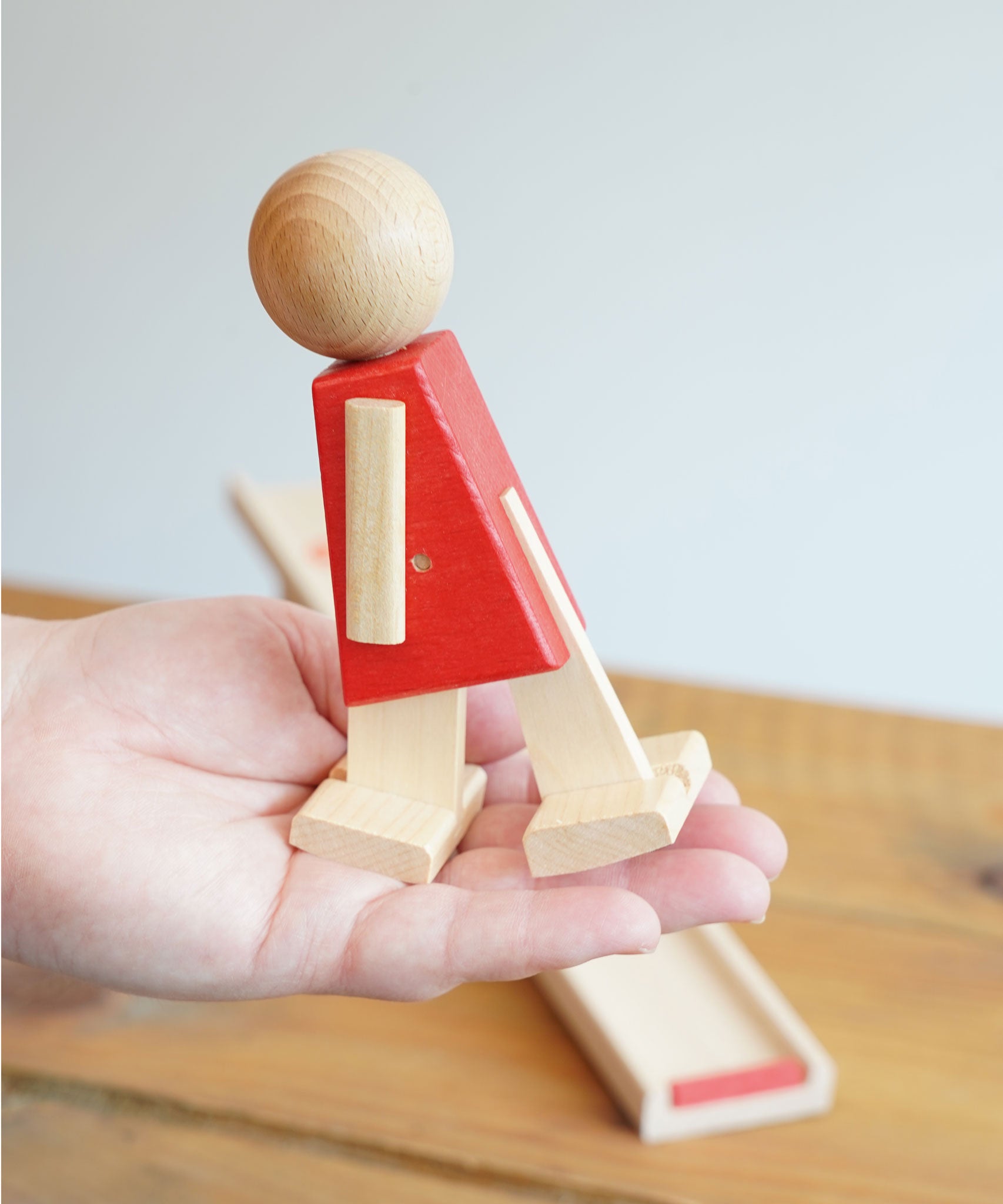 The red colour body walking figure from the Beck Toys Nurmi Ramp Walker Wooden Toy set in an adult's hand.