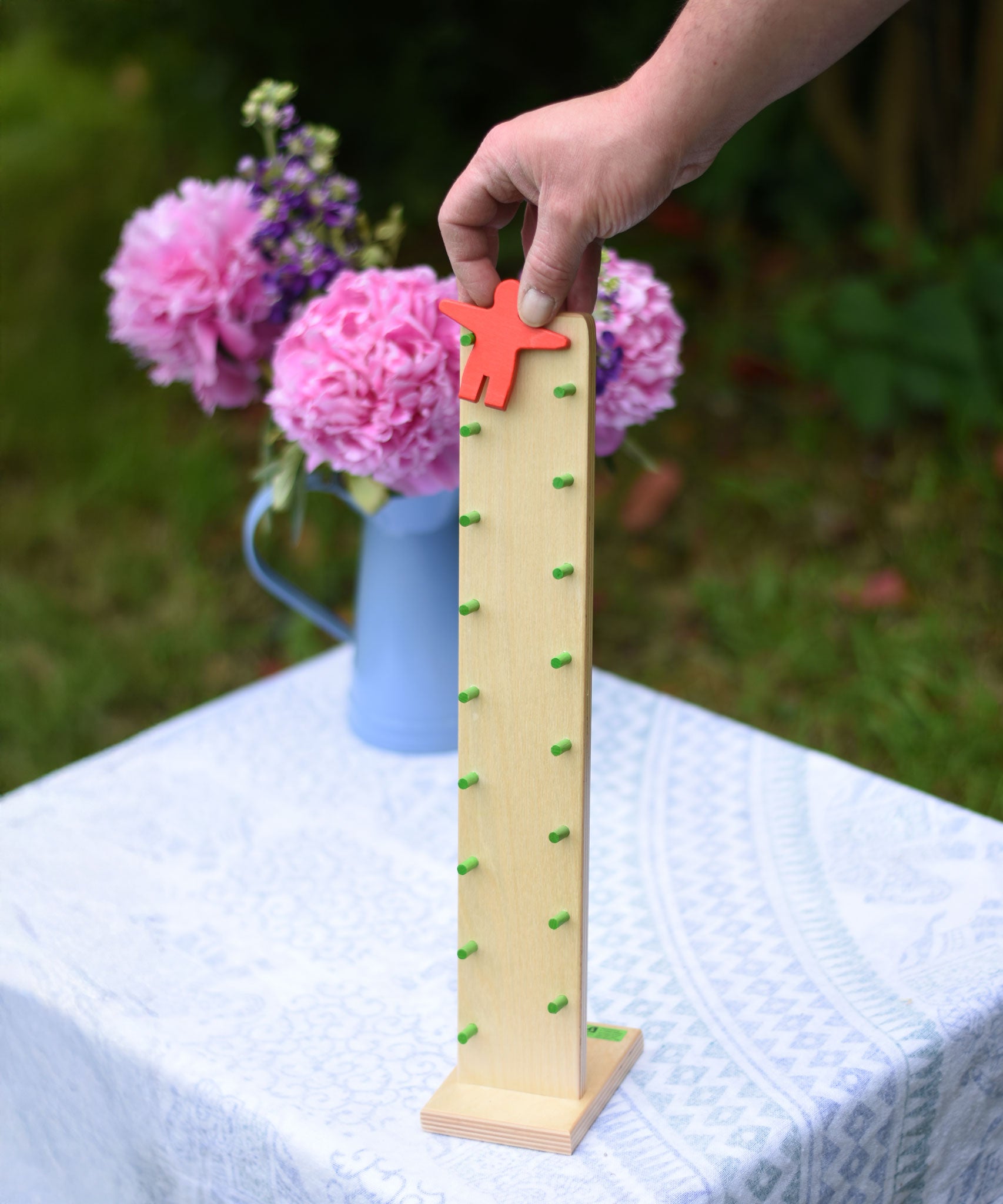 An adult's hand placing the red figure on the Beck Toys Wobbler wooden tumbling figure toy. 