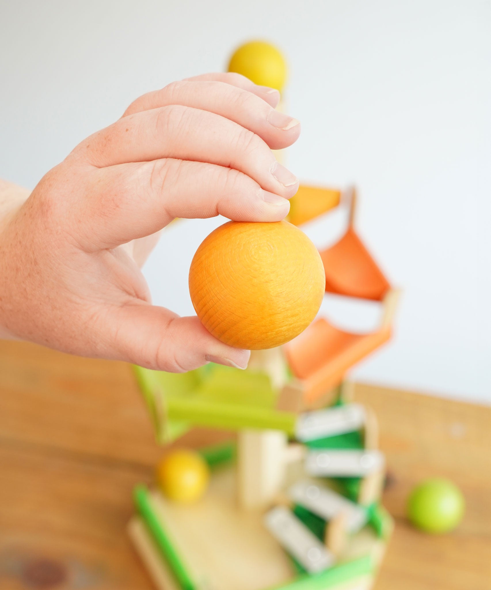 A close up of a wooden ball from the Beck Toys Beechwood Step Tower with Glockenspiel Chimes in an adult's hand. 