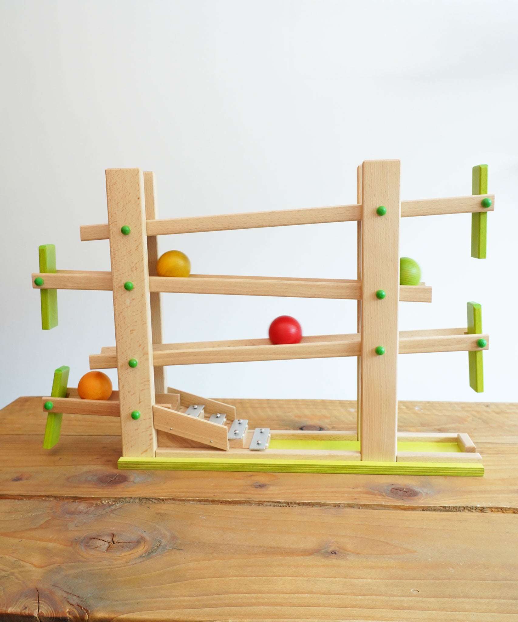 The Beck Toys Beechwood Ball Run ‘Roller Coaster Ramp’ with Glockenspiel Chimes placed on a wooden surface. The four wooden coloured balls have been set in motion on the track 