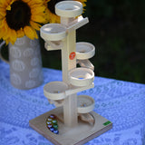 The Beck Marble Run Plate Tower placed on a small table outdoors, the 8 glass marbles are on the base of the tower. A bunch of sunflowers can be seen in the background. 