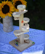 The Beck Marble Run Plate Tower placed on a small table outdoors, the 8 glass marbles are on the base of the tower. A bunch of sunflowers can be seen in the background. 