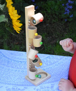 A child playing with the Beck Toys Beech Wood Roller Cup Marble Run which has been placed on a table outdoors. Glass marbles can be seen cascading down from cup to cup. 