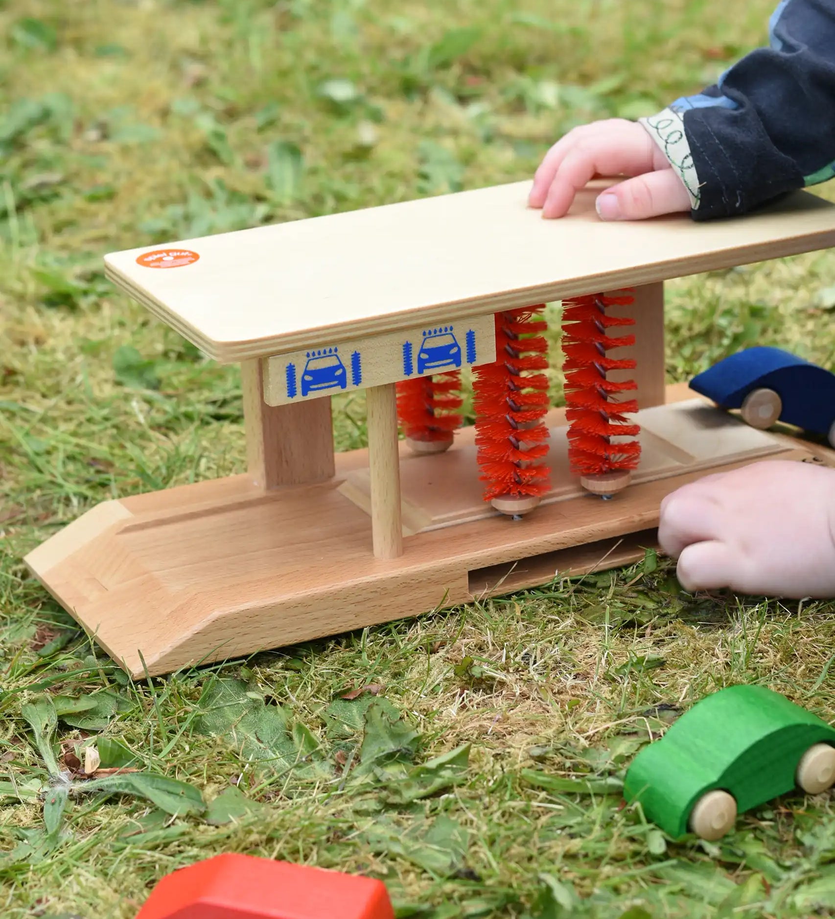 Beck wooden toy car wash being played with by a child on grass outdoors.