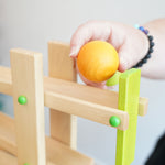 A yellow coloured wooden ball from the Beck Ball Run Musical Track in an adult's hand.