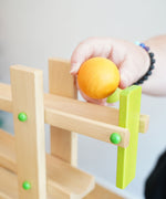 A yellow coloured wooden ball from the Beck Ball Run Musical Track in an adult's hand.