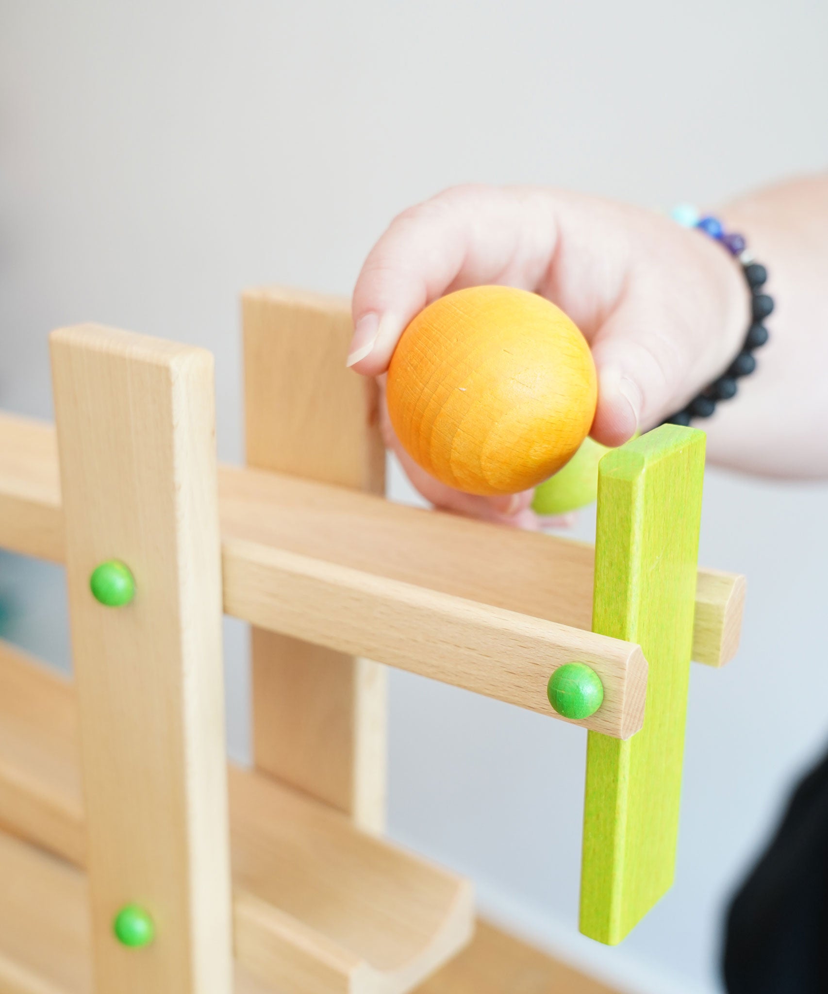 A yellow coloured wooden ball from the Beck Ball Run Musical Track in an adult's hand.