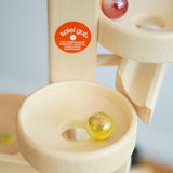 A close up of glass marbles cascading down the Beck Toys Maple Wood Marble Run Plate Tower. There is a Spiel Gut certification sticker on the tower. 