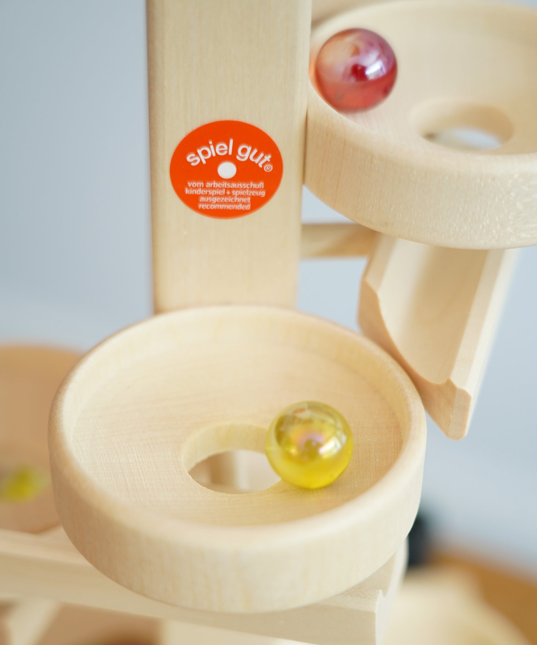 A close up of glass marbles cascading down the Beck Toys Maple Wood Marble Run Plate Tower. There is a Spiel Gut certification sticker on the tower. 