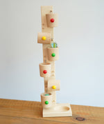 The Beck Toys Beech Wood Roller Cup Marble Run placed on a wooden surface. A glass marble can be seen blurred in motion whilst flowing from one cup to the one underneath. 