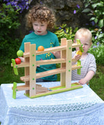 Two children playing with the Beck Ball Run Musical Track which has been placed on a small table outdoors. 